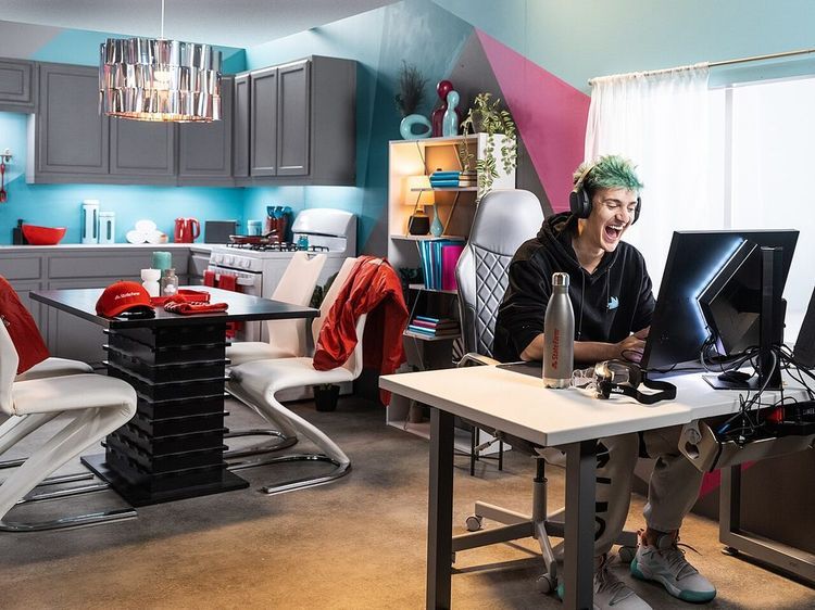 A streamer with green hair and headphones laughs while playing on a computer in a brightly colored apartment set.